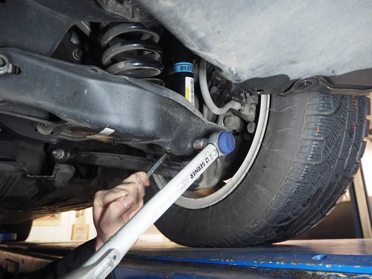 Ręka dokręca śrubę kluczem dynamometrycznym, pokazując, jak zamontować amortyzatory do przyczepki.