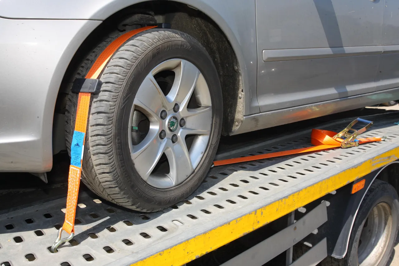 Pomarańczowa taśma zabezpiecza koło auta na lawecie, zapewniając bezpieczne mocowanie pojazdu podczas transportu.