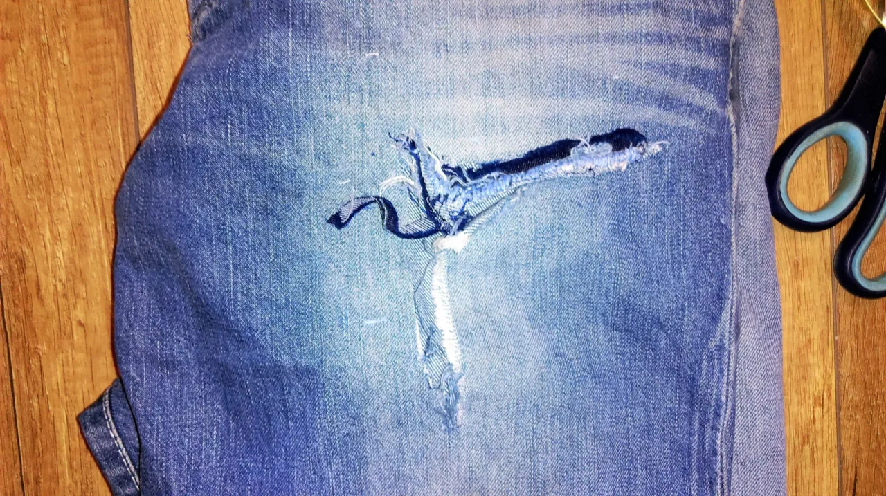 Jak zaszyć dziurę w spodniach? Widok na podarte jeansy i nożyczki, gotowe do naprawy.