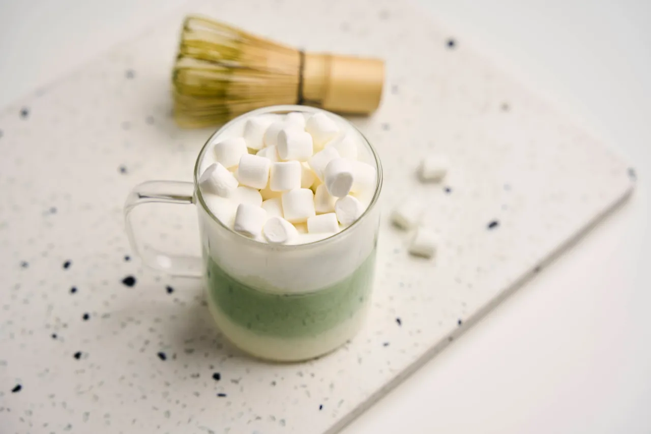 Kremowe matcha latte z piankami marshmallow. Tradycyjny bambusowy chasen obok, sugerujący jak pić matcha.