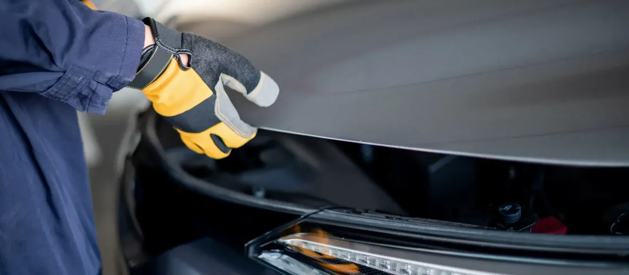 Ręka w rękawicy zamyka maskę samochodu. Co jeśli samoch&oacute;d nie przejdzie przeglądu? Czas na wizytę u mechanika.