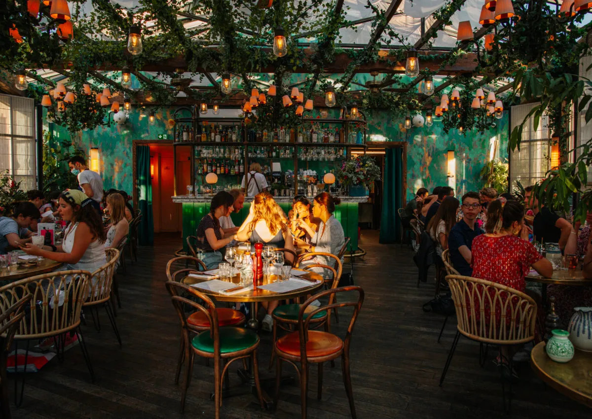 W paryskiej restauracji z zielonymi ścianami i roślinnością na suficie ludzie jedzą obiad. Ile kosztuje obiad w Paryżu? Trudno powiedzieć, ale atmosfera jest wspaniała.