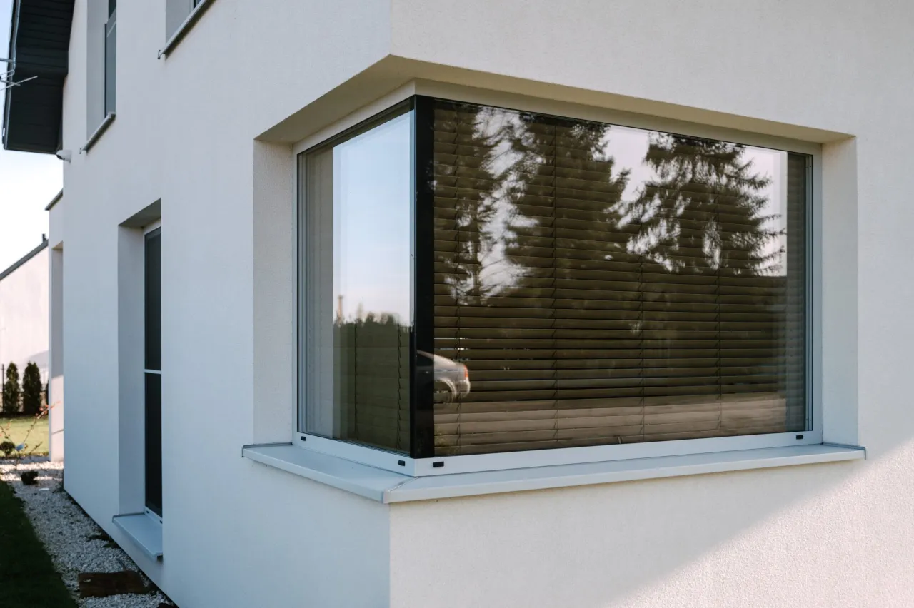 Nowoczesne okno narożne ze słupem betonowym, z żaluzjami i odbiciem samochodu.