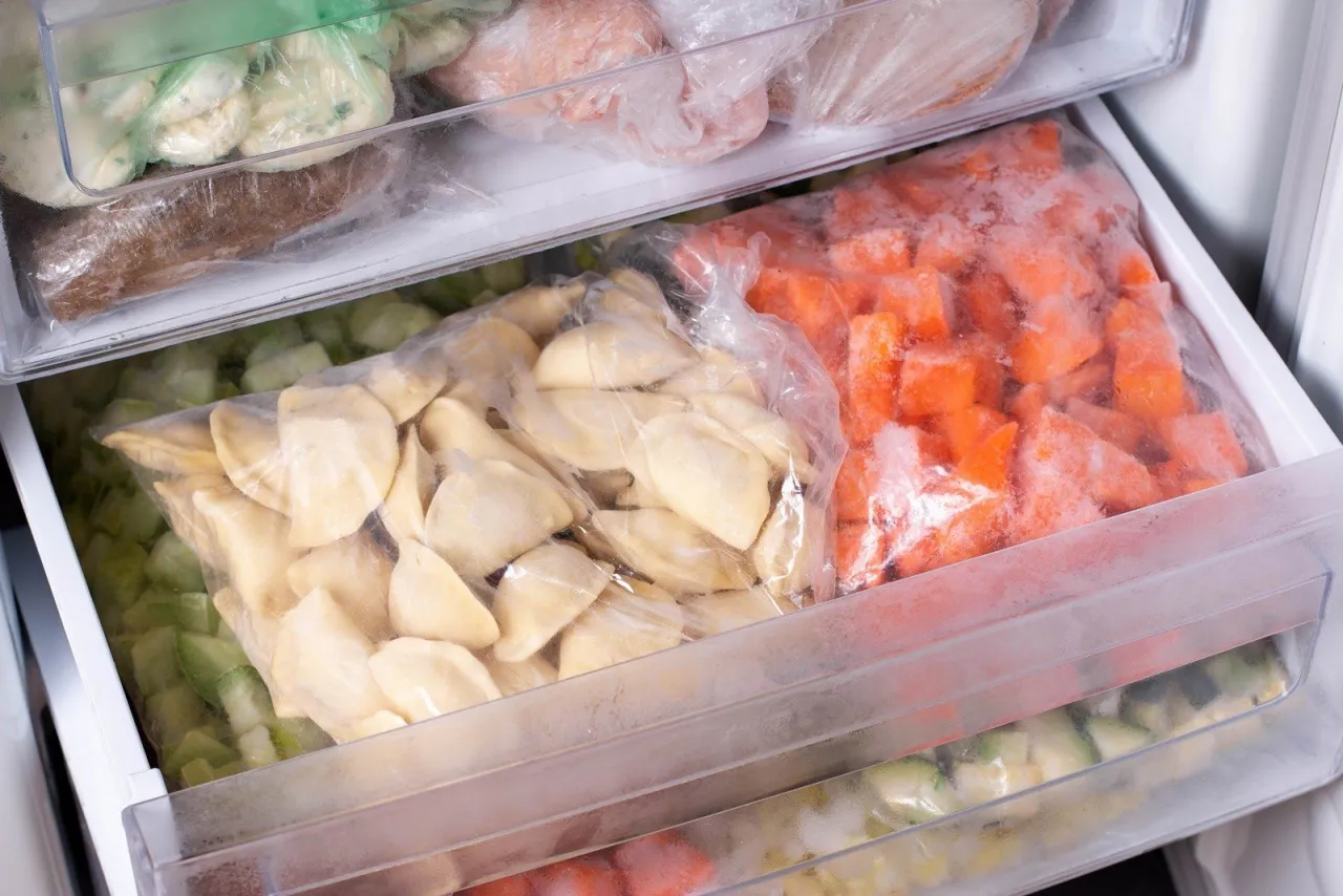 Zamrożone pierogi w woreczku, obok pokrojonej marchewki i cukinii. To świetny spos&oacute;b, jak mrozić pierogi na p&oacute;źniej.