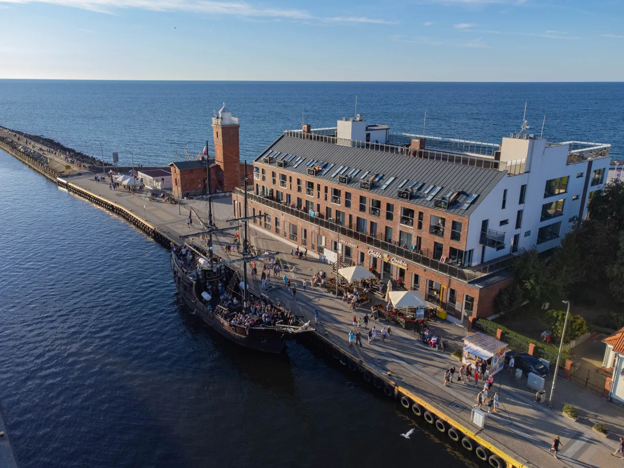 Port z latarnią morską, hotelem i statkiem pirackim. Zastanawiasz się, ile kosztuje nocleg nad morzem w takim miejscu?