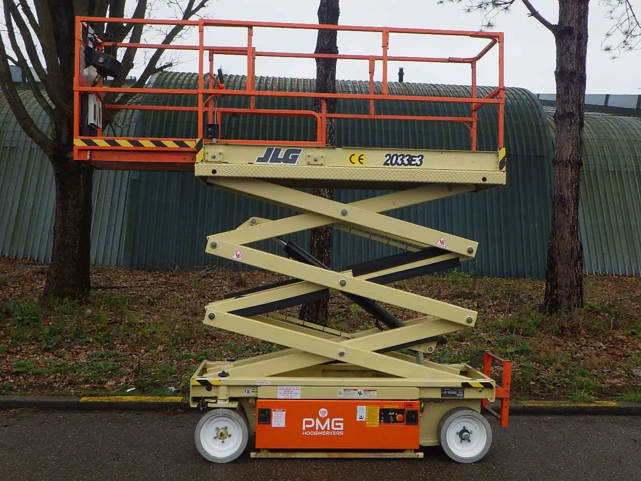 Podnośnik nożycowy JLG w kolorze beżowym i pomarańczowym. Zastanawiasz się, ile kosztuje godzina pracy zwyżki?