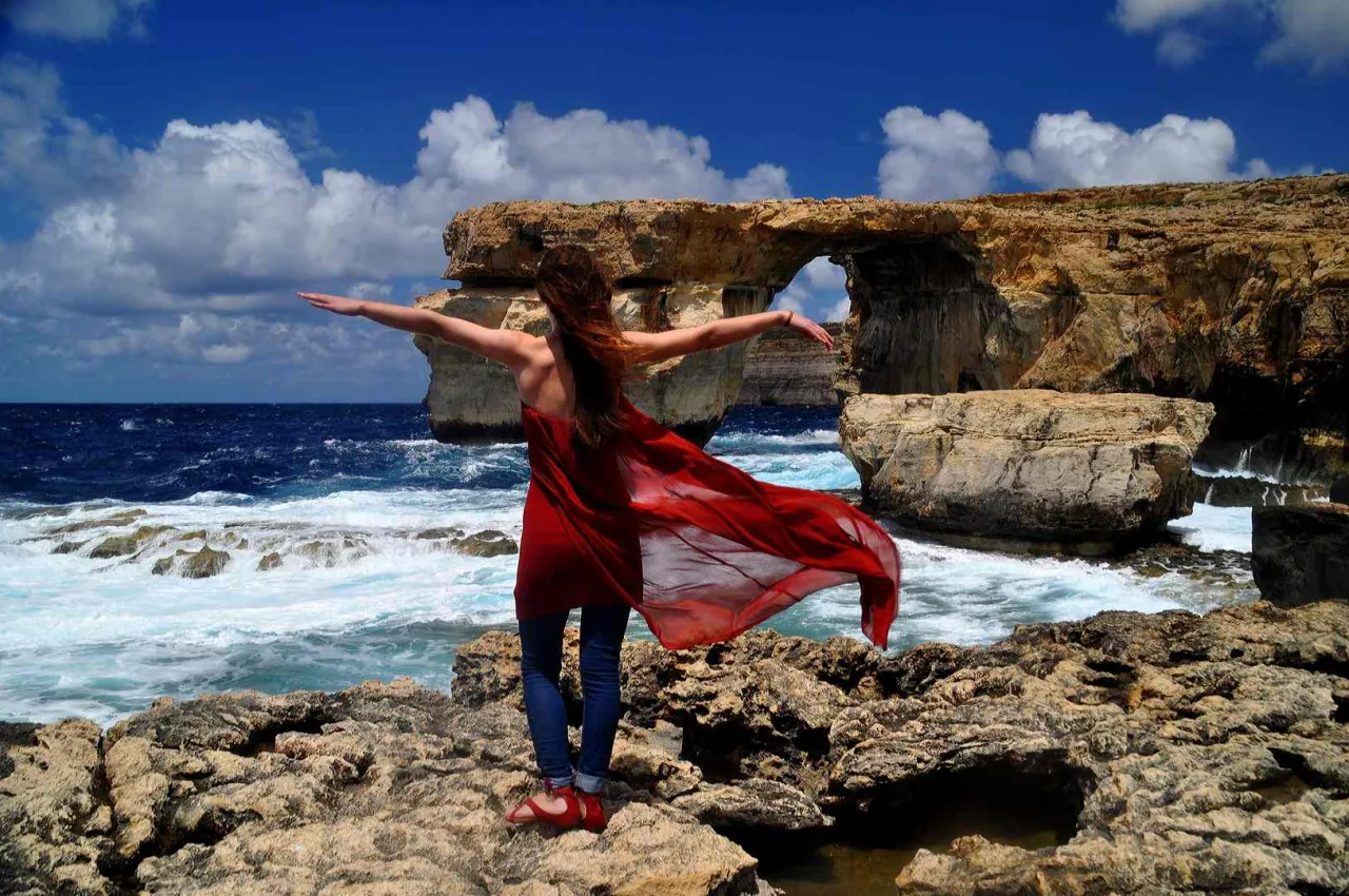 Kobieta w czerwonej sukience na maltańskich klifach. W marcu na Malcie jest cieplej niż na Cyprze.