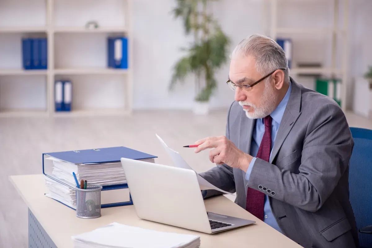 Starszy mężczyzna w garniturze analizuje dokumenty, zastanawiając się, kto nie płaci funduszu pracy.
