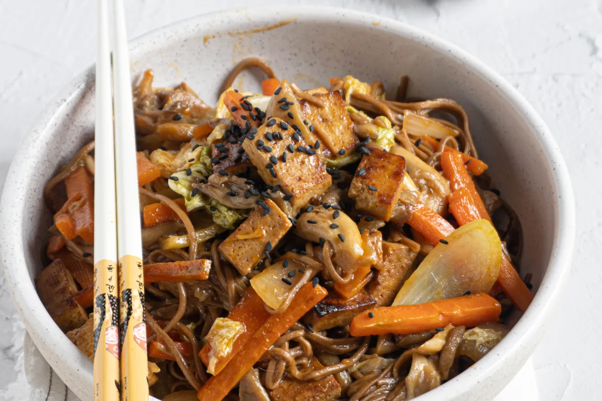Pyszne makaron z tofu po azjatycku z warzywami i czarnym sezamem, gotowy do jedzenia pałeczkami.