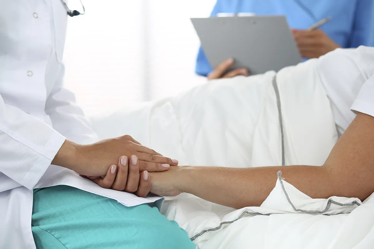 Lekarz w białym kitlu trzyma dłoń pacjenta, który leży w łóżku. To pokazuje, jaki lekarz nie może poślubić swojej pacjentki.