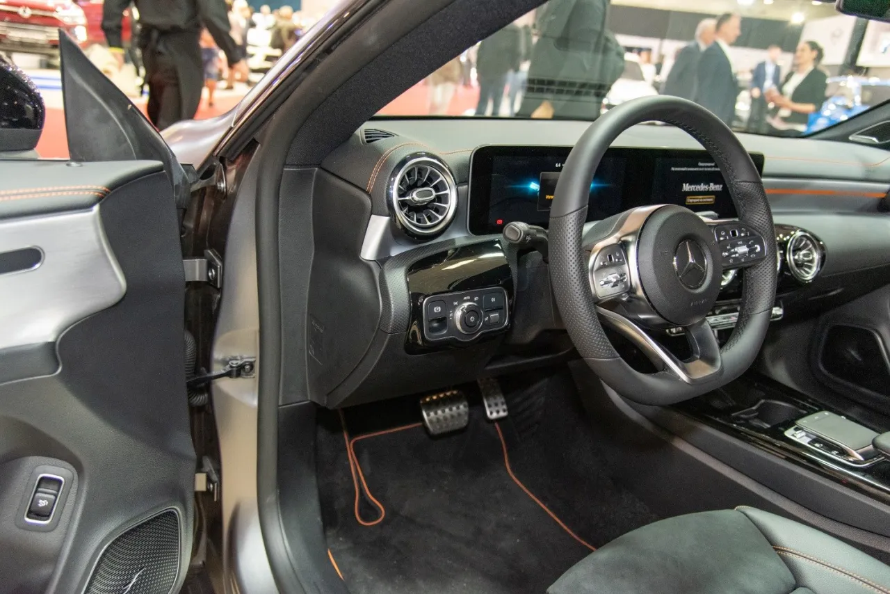 Wnętrze Mercedesa CLA: kierownica, deska rozdzielcza z ekranem i nawiewami, pedały.