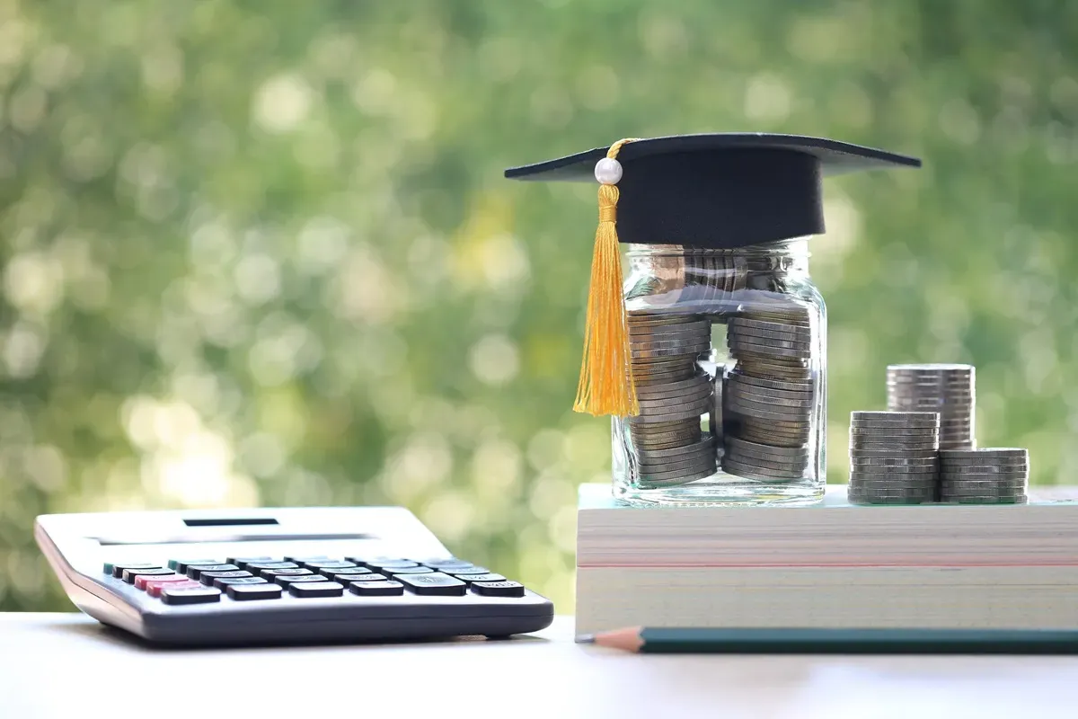 Słoik z monetami i czapką absolwenta, obok kalkulator i stos książek. Czy nagroda jubileuszowa wlicza się do emerytury?