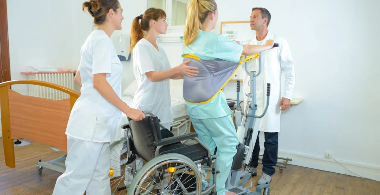 Fizjoterapeuta pomaga pacjentowi wstać po operacji, wczesna pionizacja