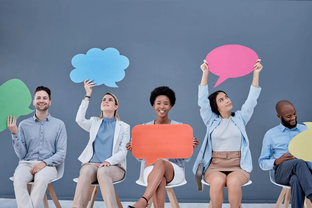 Ludzie siedzą w rzędzie, trzymając kolorowe dymki, symbolizujące ich potrzeby w związku.