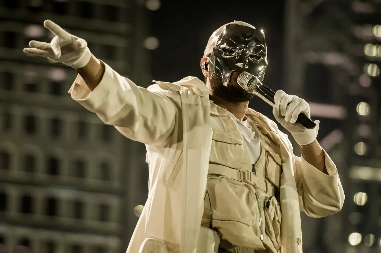 Artysta w masce i białej kurtce śpiewa do mikrofonu, wskazując palcem. Zastanawiasz się, ile trwa koncert The Weeknd?