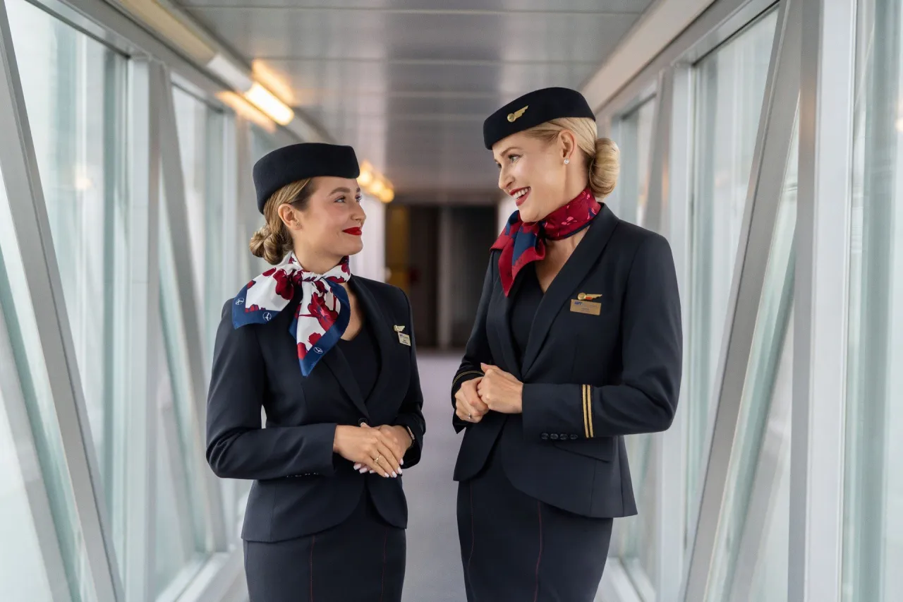 Dwie stewardessy w eleganckich mundurkach rozmawiają na lotnisku. Ciekawe, ile zarabia steward w lot.