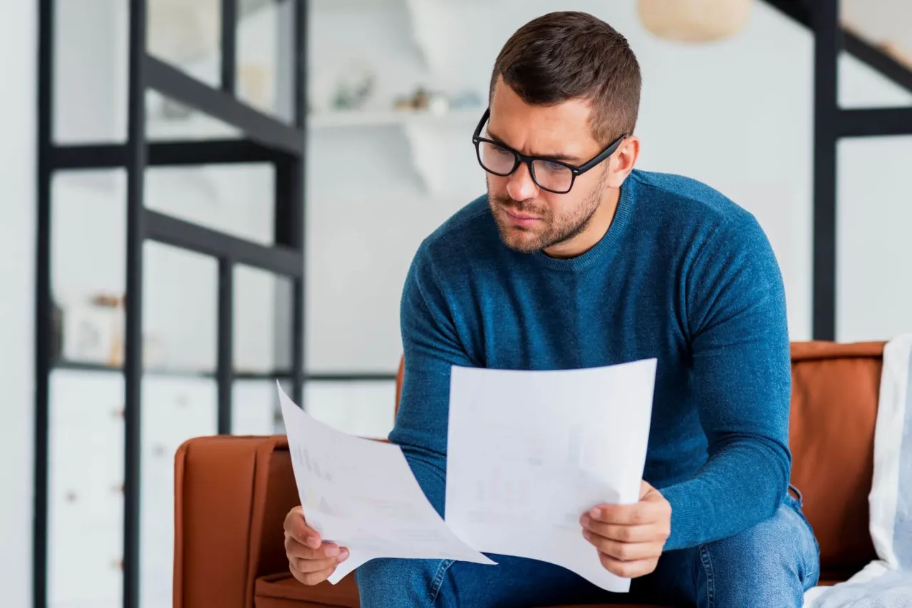 Mężczyzna w okularach analizuje dokumenty, szukając informacji, jak sprawdzić BIK osoby zmarłej.