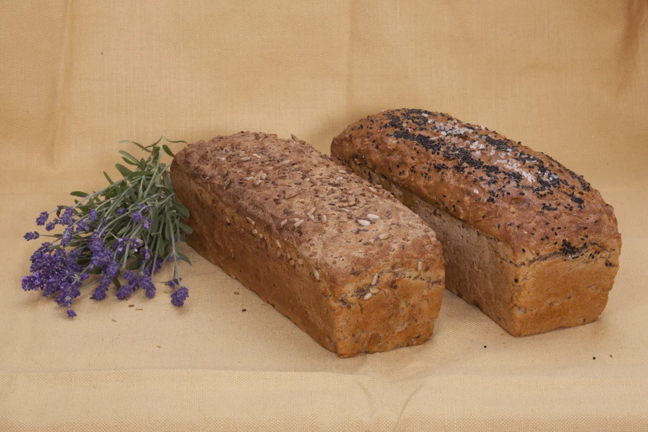Dwa bochenki chleba żytniego, jeden z nasionami słonecznika, drugi z czarnuszką i solą. Obok gałązka lawendy. Czy chleb żytni powoduje wzdęcia?