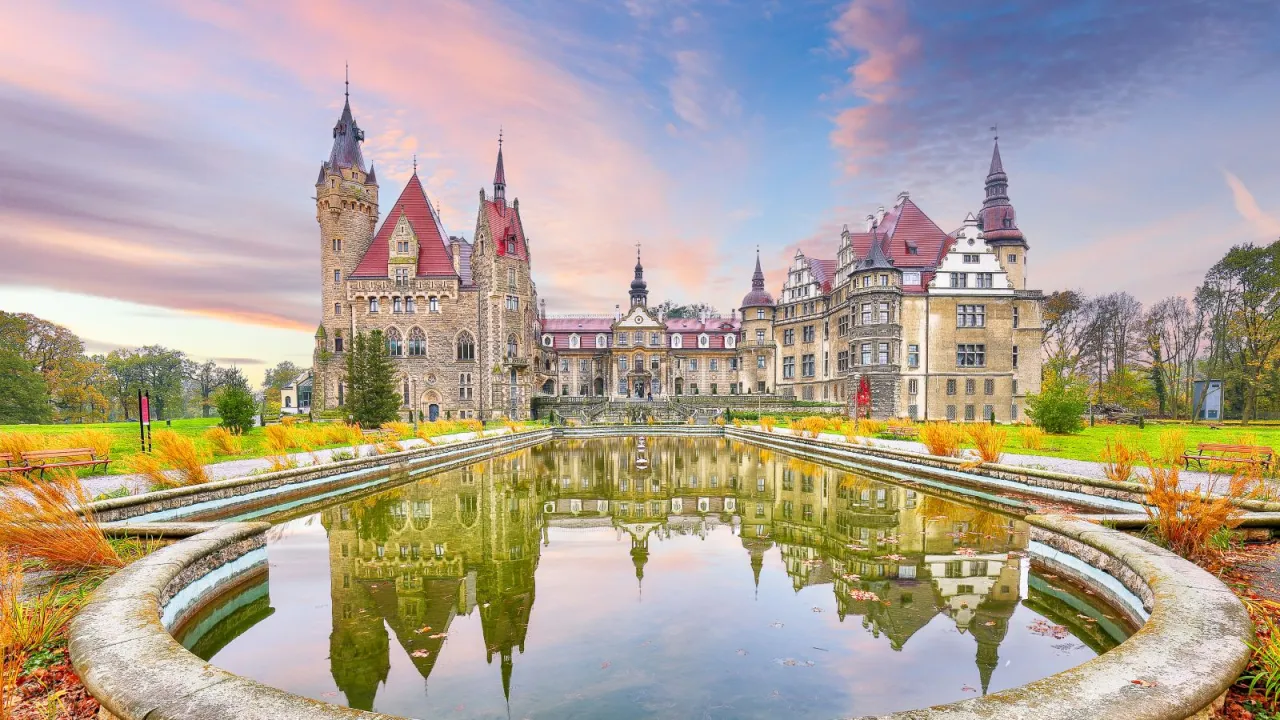 Bajkowy Zamek Moszna odbija się w stawie. Zastanawiasz się, ile trwa zwiedzanie zamku Moszna? Warto zaplanować co najmniej kilka godzin!