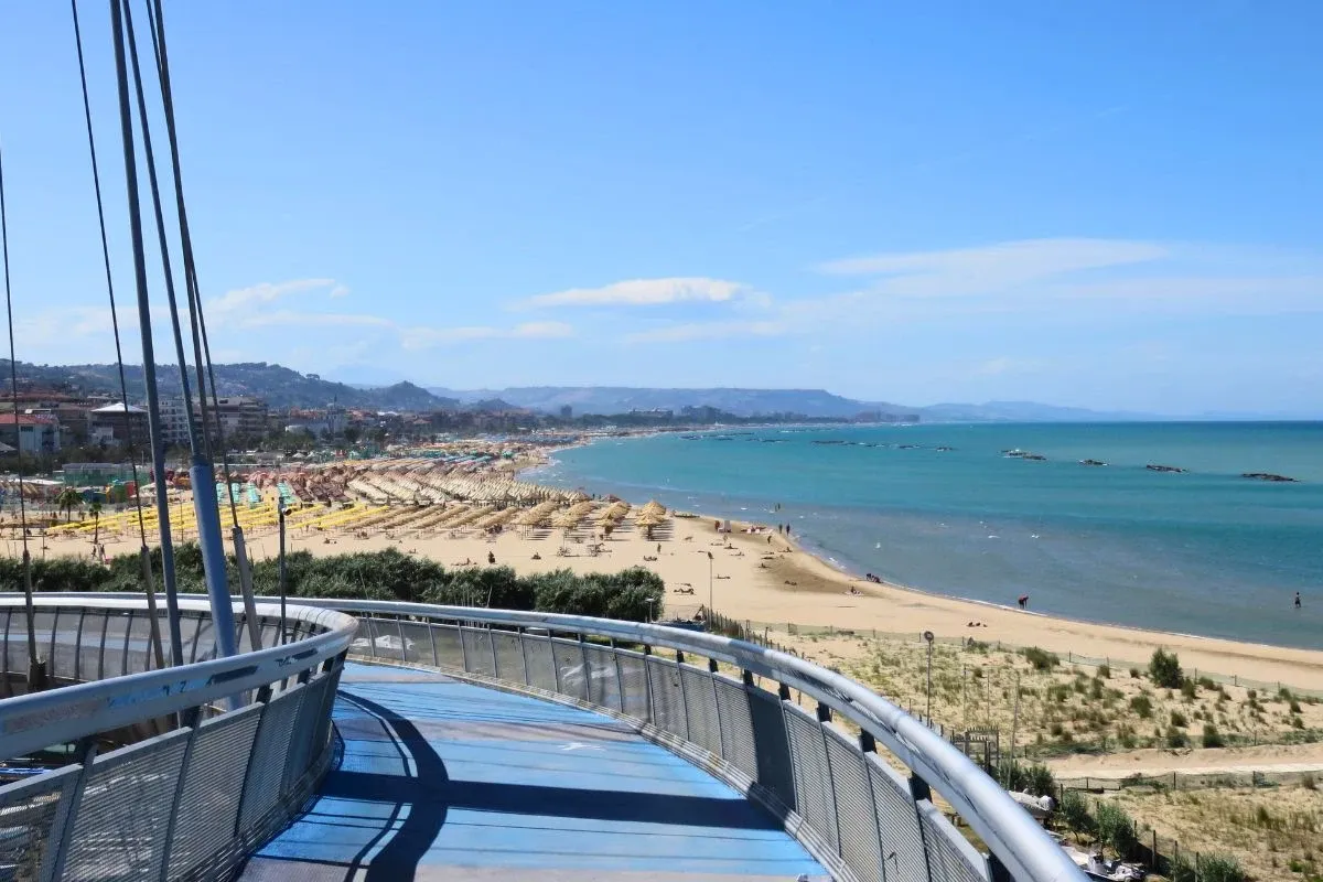Widok na plażę w Pescara z nowoczesnego mostu. Słoneczny dzień, turkusowe morze, rzędy parasoli i leżaków. Idealne miejsce, by zobaczyć, co zobaczyć w Pescara.