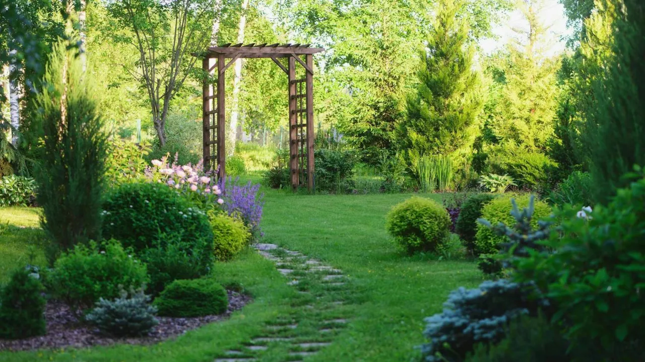 Piękny ogród z kamienną ścieżką prowadzącą do drewnianej pergoli. Inspiracja, jak zbudować pergolę, by stworzyć magiczne miejsce.