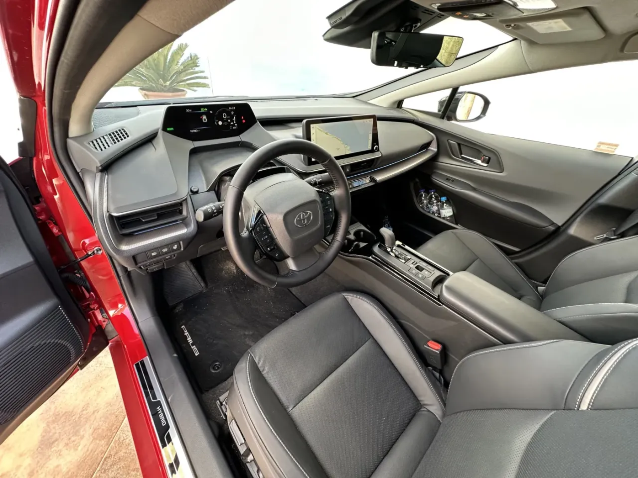 Wnętrze Toyoty Prius, z widocznymi przednimi fotelami i konsolą. Auto oferuje komfortowe miejsca dla pasażer&oacute;w.