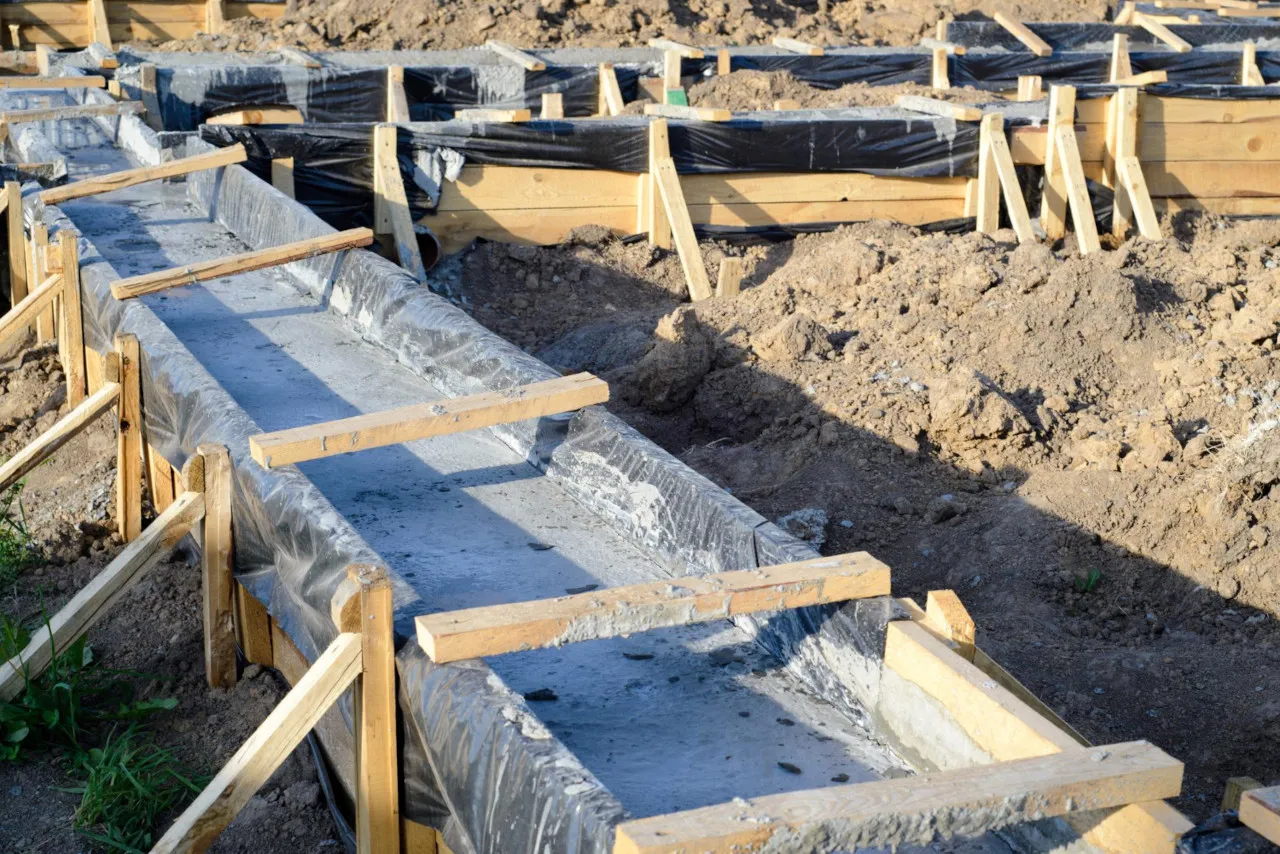 Świeżo wylane betonowe ławy fundamentowe w drewnianym szalunku. Czekają, aż ile muszą odstać fundamenty, by można było kontynuować budowę.