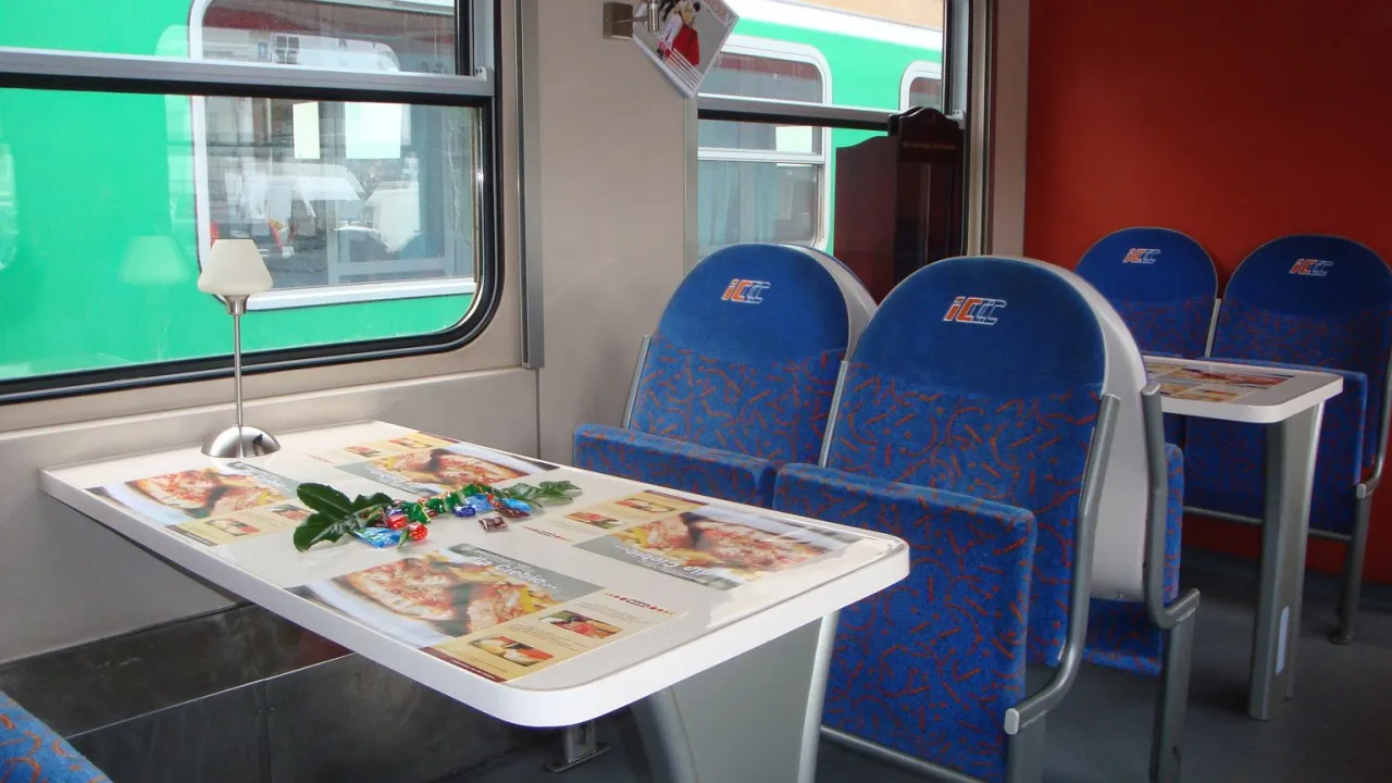 Wnętrze wagonu restauracyjnego PKP Intercity. Stolik z menu pizzy i lampką. Jak sprawdzić czy w pociągu jest wars?