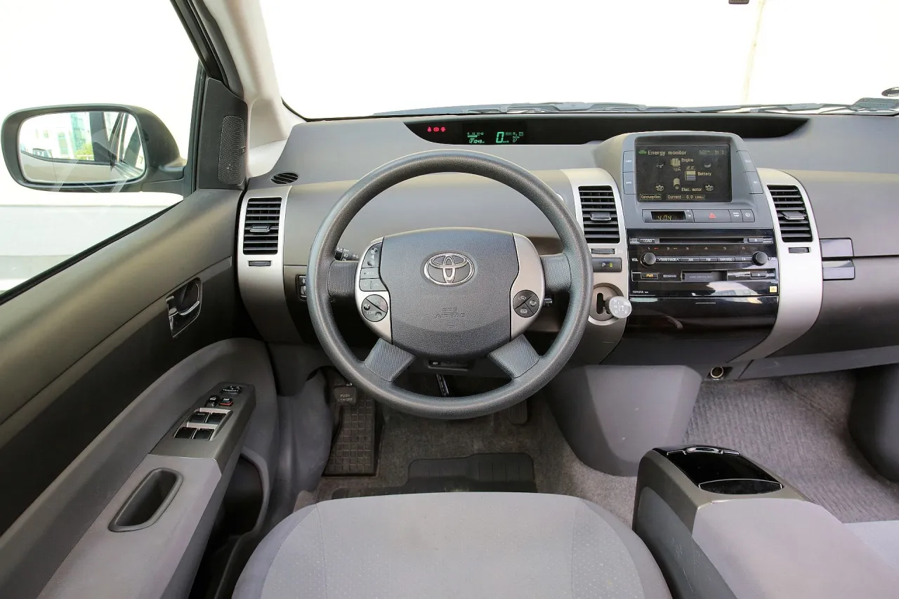 Wnętrze Toyoty Prius. Czy warto kupić ten hybrydowy samoch&oacute;d? Kierownica, deska rozdzielcza z ekranem i radiem.