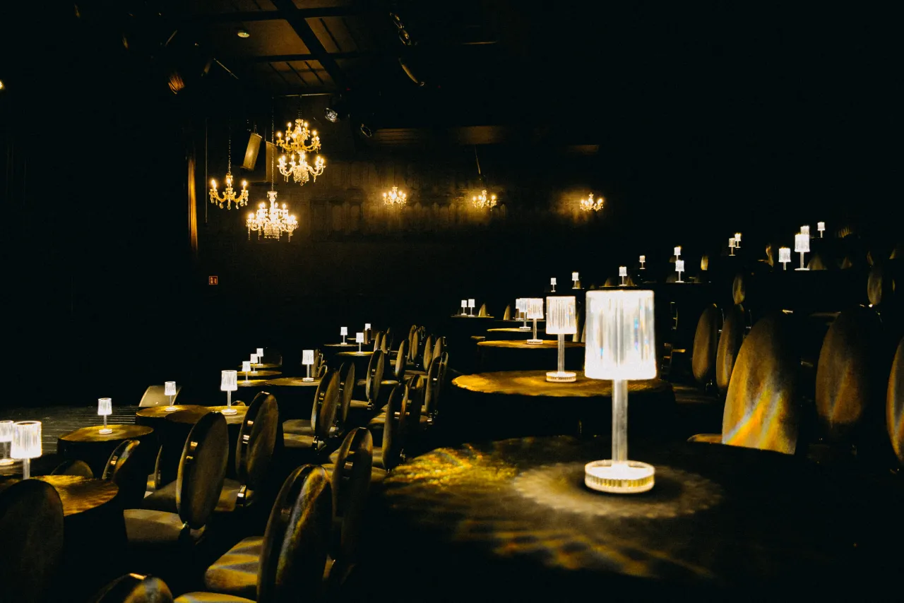 Eleganckie wnętrze z żyrandolami i stolikami, przypominające scenę teatralną. Takie miejsca w Warszawie oferują niezapomniane wrażenia.