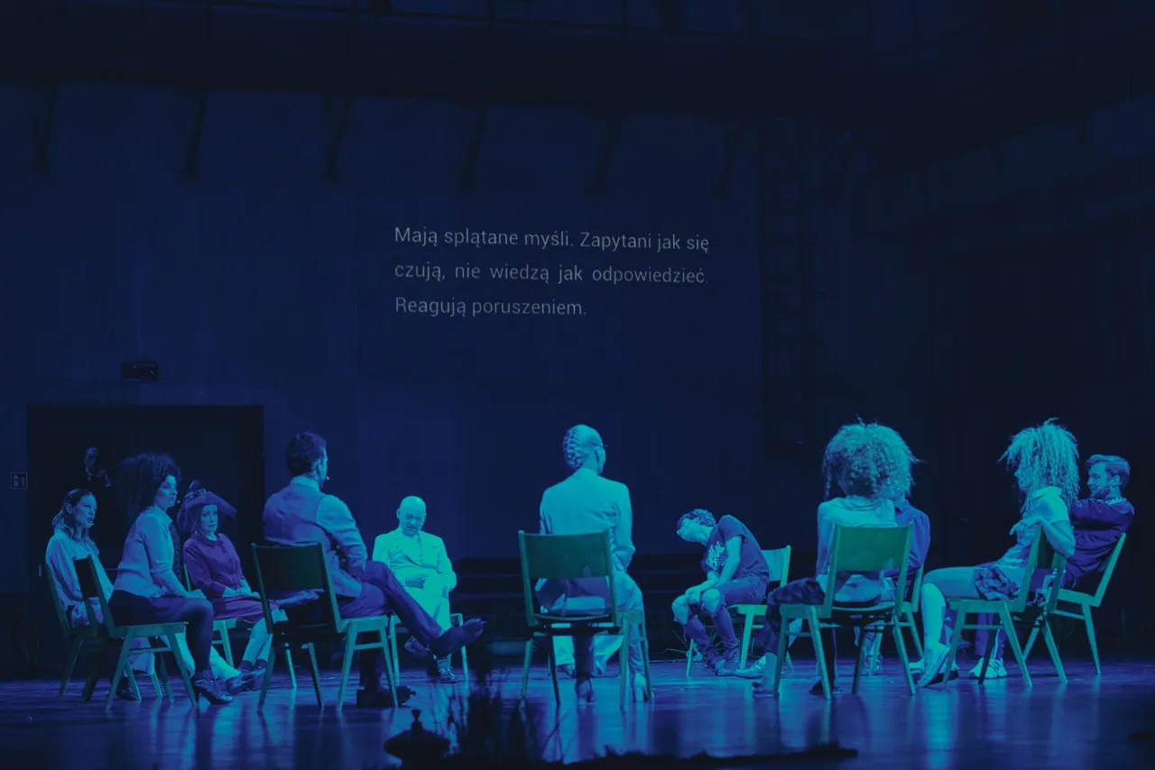 Grupa ludzi na scenie, wpatrzona w ekran z tekstem. Teatr pokazuje, po co jest: by zadawać pytania, na które nie zawsze znamy odpowiedź.