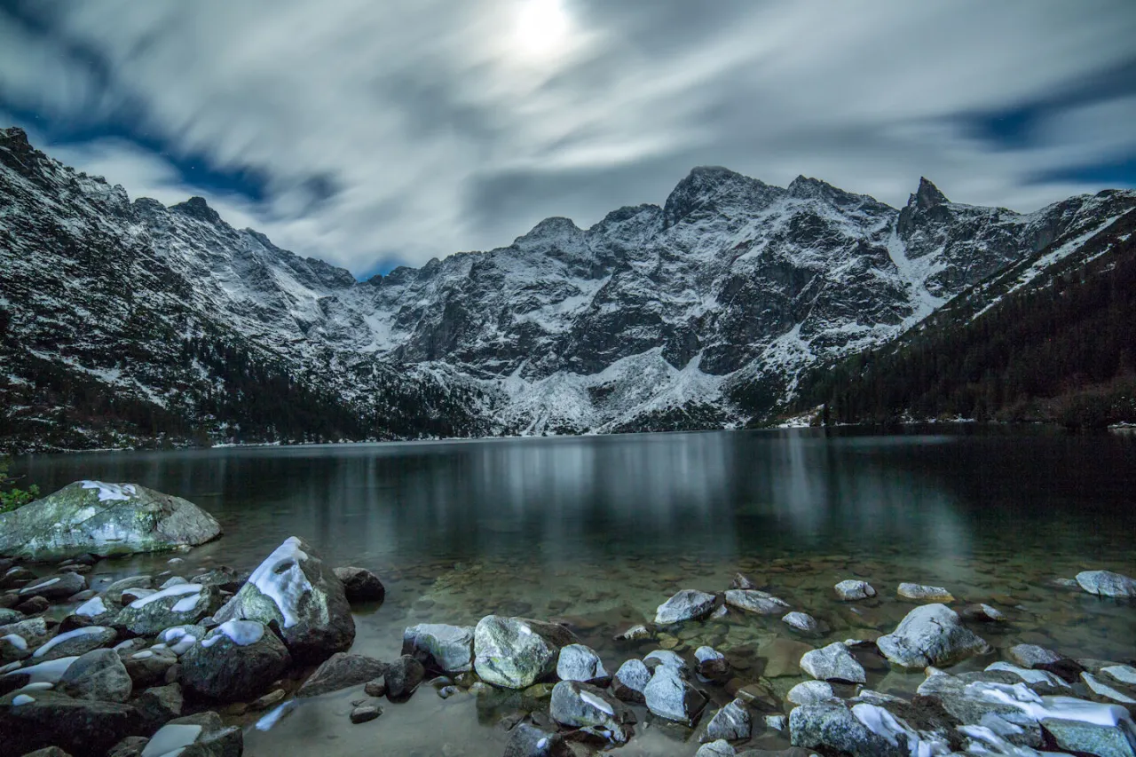 Morskie Oko nocą, góry w śniegu, chmury na niebie. Zastanawiasz się, ile kosztuje nocleg w schronisku nad Morskim Okiem?