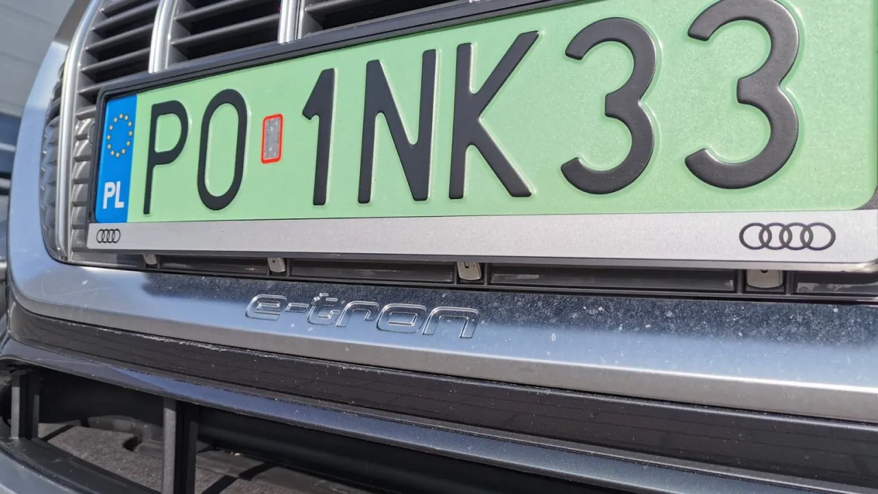 Zielona tablica rejestracyjna PO 1NK33 z symbolem PL i logo Audi. Pod nią napis e-tron.
