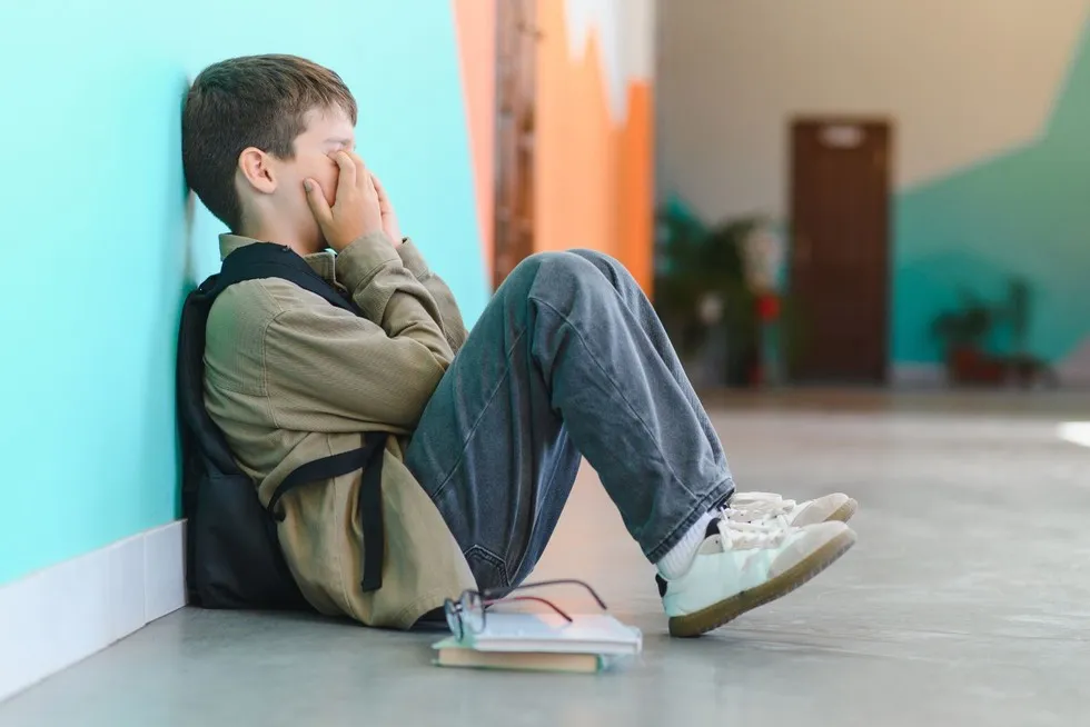 smutne dziecko siedzące samotnie na szkolnym korytarzu