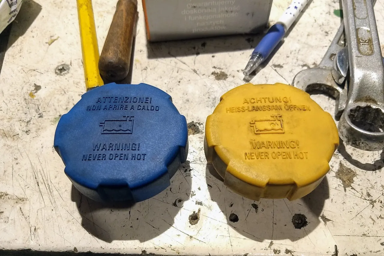 Dwa korki układu chłodzenia, jeden niebieski, drugi ż&oacute;łty, ostrzegają przed otwieraniem gorącego systemu. Mogą to być przyczyny wysokiego ciśnienia w układzie chłodzenia.