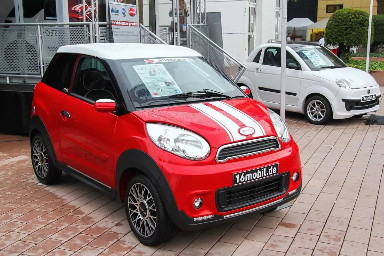 Czerwony pojazd samochodowy inny, jakie prawo jazdy? Obok biały samoch&oacute;d. Oba na wystawie.