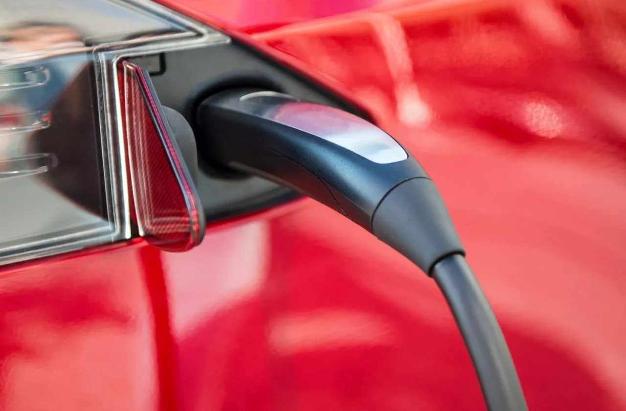 Ładowarka podłączona do czerwonej Tesli. Zastanawiasz się, jak długo ładuje się Tesla? Czas zależy od ładowarki i modelu.