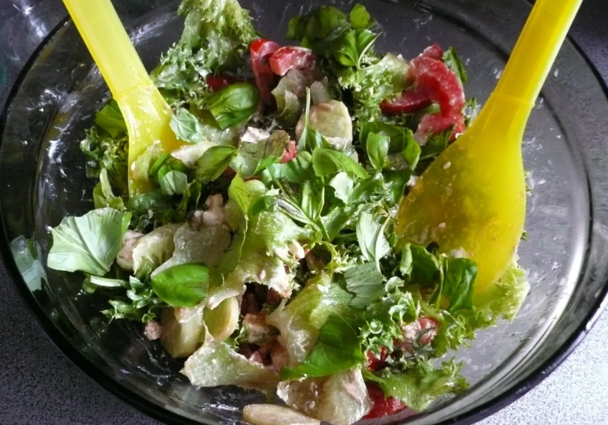 Sałatka z pomidorami i bazylią, kt&oacute;ra dodaje świeżości i aromatu. Dwie ż&oacute;łte łopatki mieszają składniki.