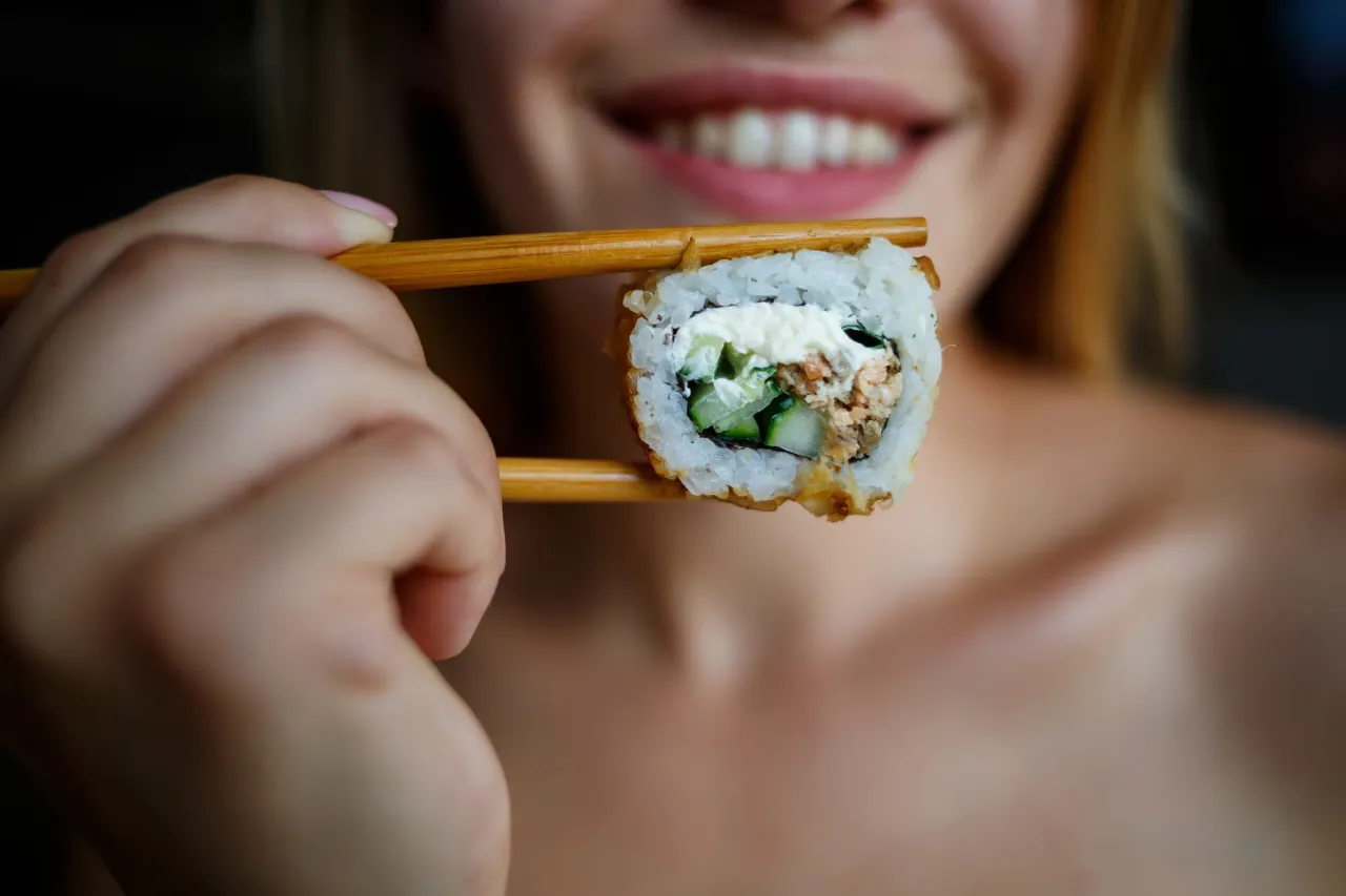 Uśmiechnięta kobieta trzyma pałeczkami sushi z łososiem i ogórkiem. Czy można jeść sushi karmiąc piersią?