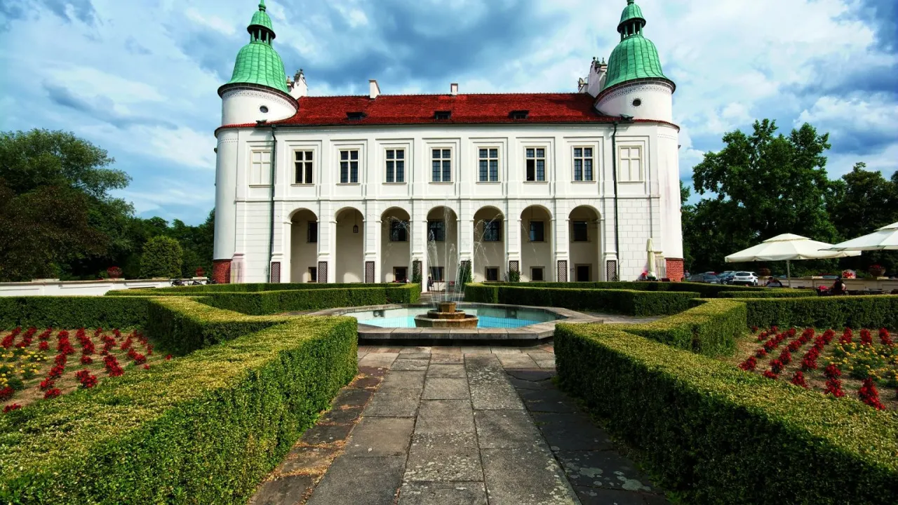 Pałac z arkadowym podcieniem i fontanną, ogród z żywopłotami i rabatami kwiatowymi. Klasyczne cechy sztuki renesansowej widoczne w architekturze.