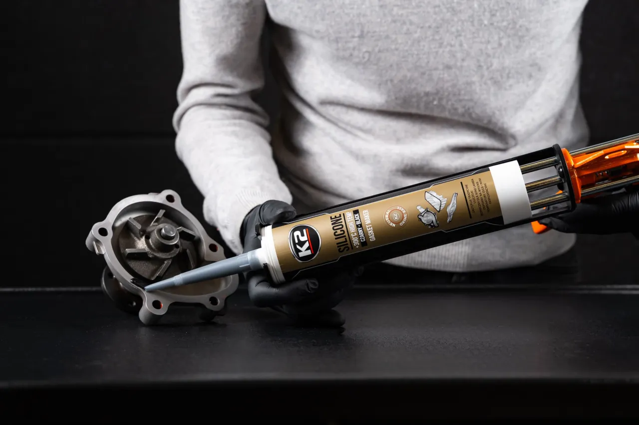 Ręce w czarnych rękawiczkach aplikują czarny silikon na wysokie temperatury na element pompy wodnej.