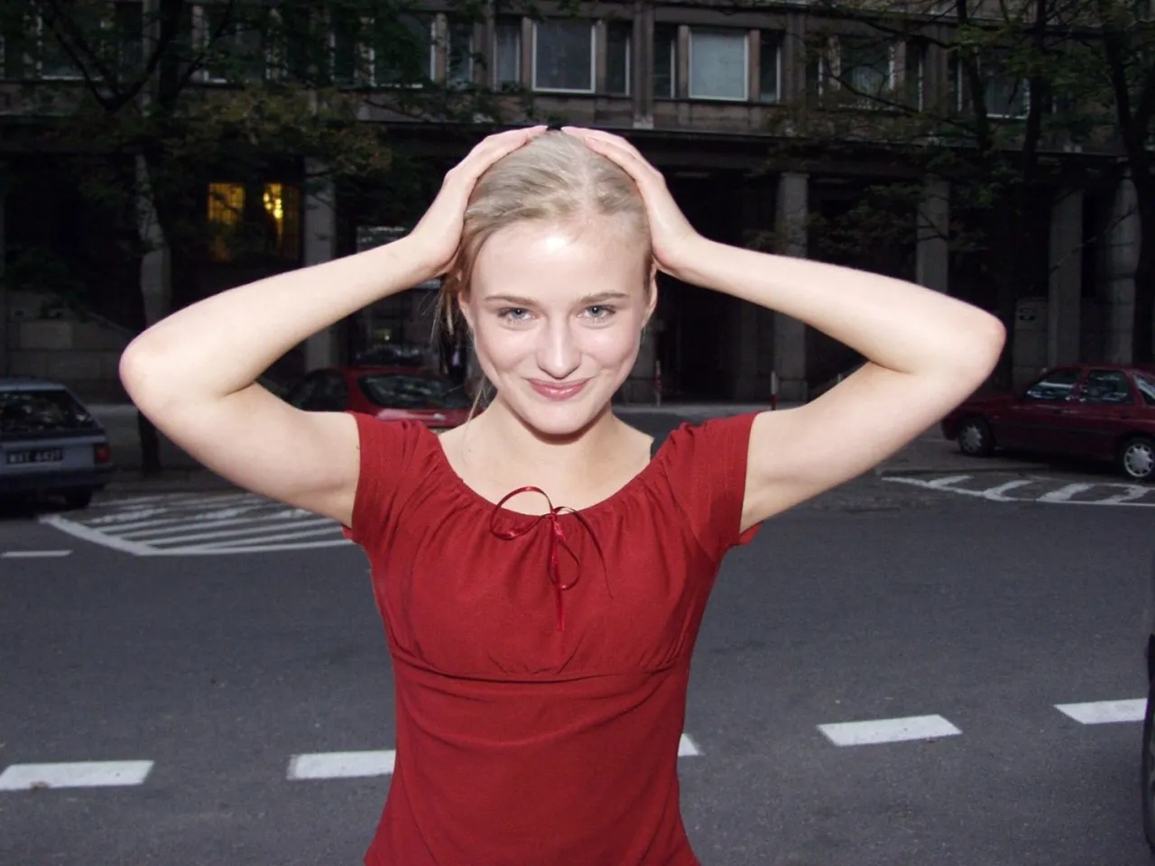 Marta Chodorowska z uśmiechem, ręce na głowie. W tle budynek i samochody.