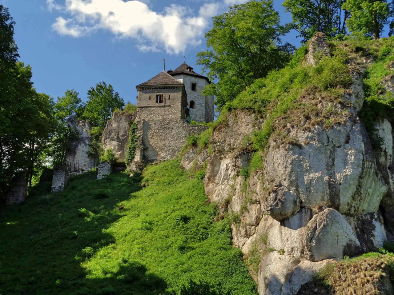 Zamek na skale, idealny punkt widokowy na ojców trasę rowerową. Zielone zbocze i błękitne niebo.