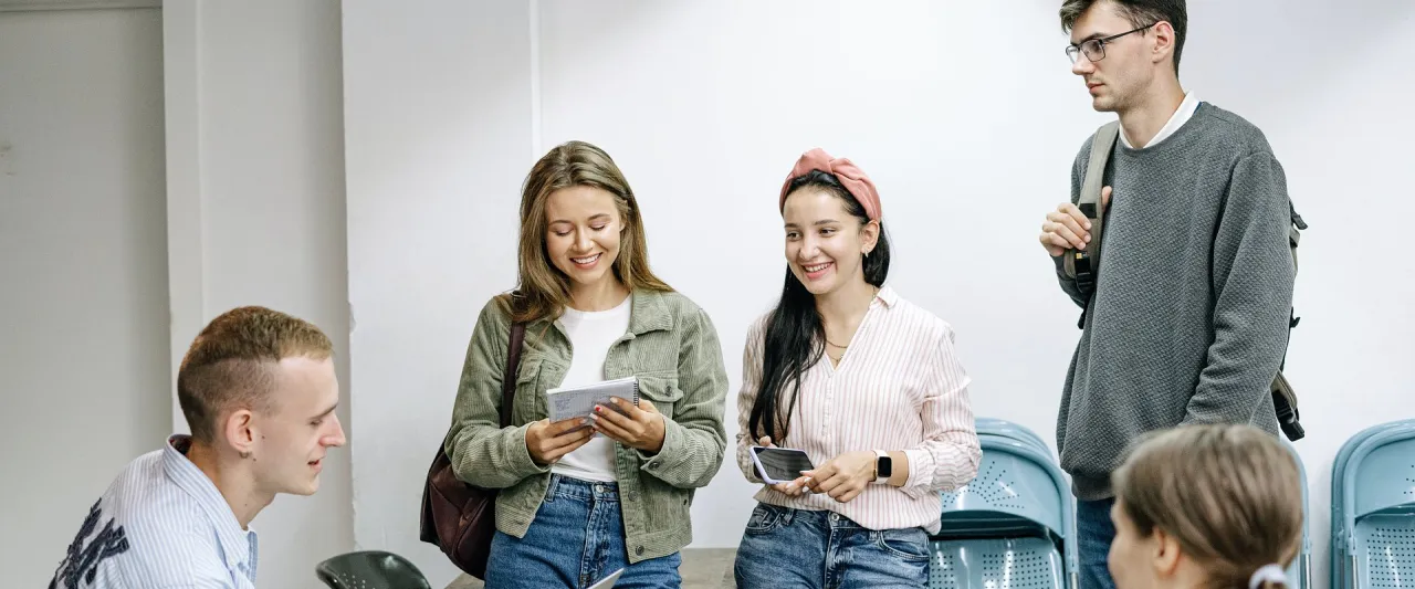 Grupa młodych ludzi dyskutuje, jak przygotować się do pracy w branży marketingowej. Uśmiechnięci, z notatnikami i telefonami, planują swoją przyszłość.