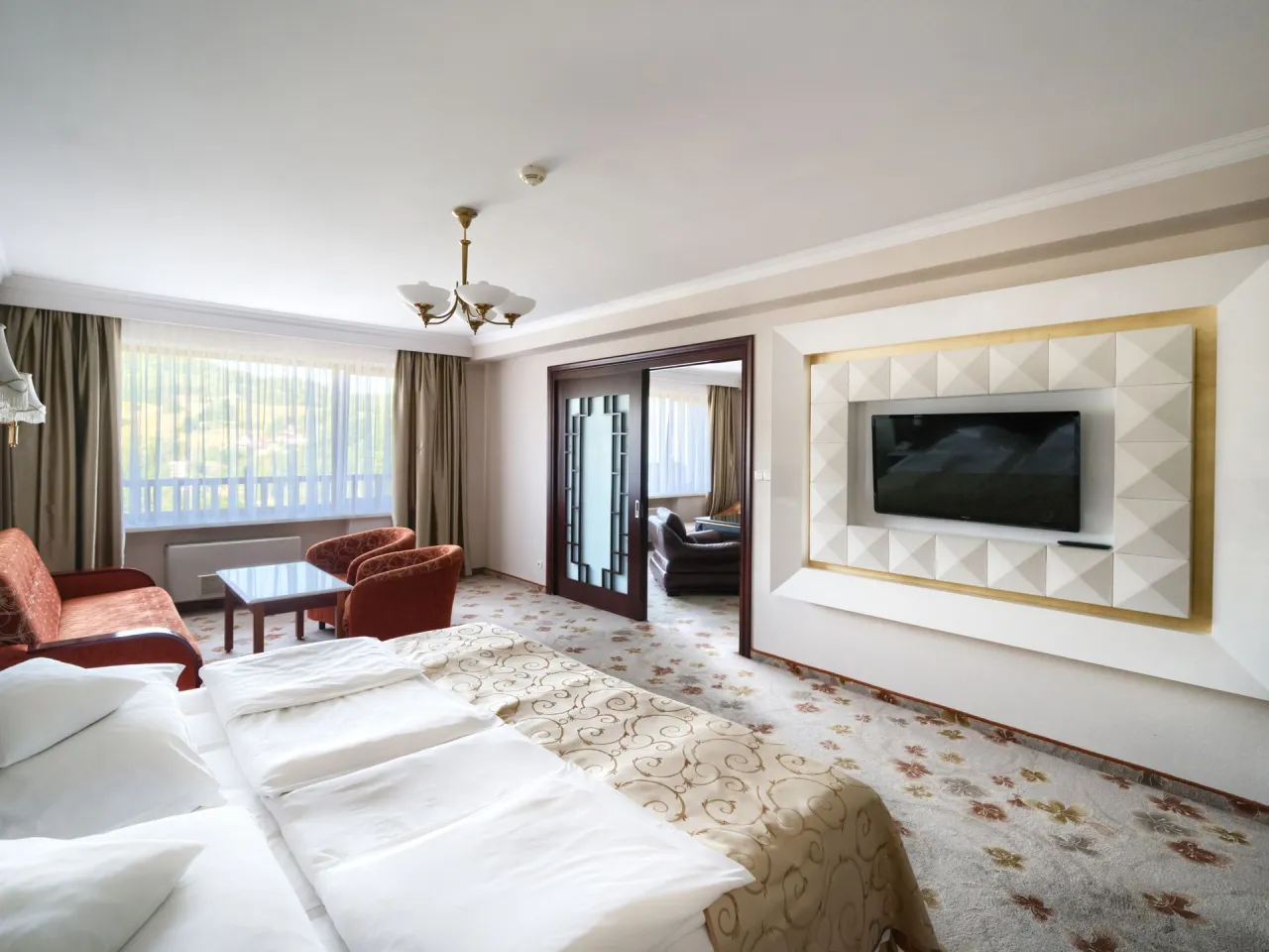 Pokój hotelowy z dużym łóżkiem, kanapą, fotelem i TV. Zastanawiasz się, ile kosztuje doba w hotelu Gołębiewski dla dwóch osób?