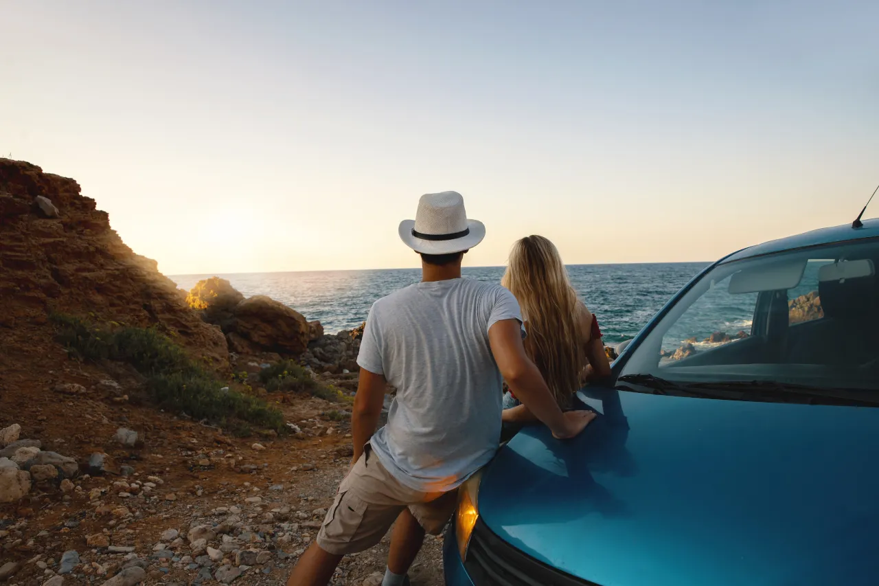 Para, kt&oacute;ra wybrała się autem na wakacje, podziwia zach&oacute;d słońca nad morzem.