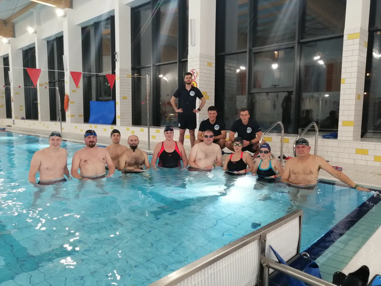 Grupa dorosłych w basenie, gotowa na naukę pływania. Od czego zacząć? Od uśmiechu i dobrej zabawy!