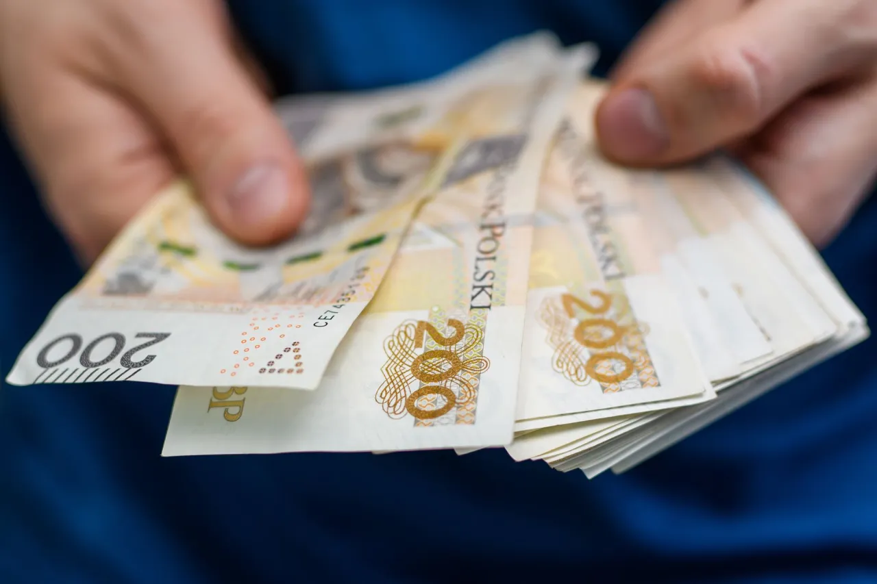 Dłonie trzymające plik banknot&oacute;w 200 zł. Może to być związane z zajęciem komorniczym, gdy pieniądze są przekazywane.