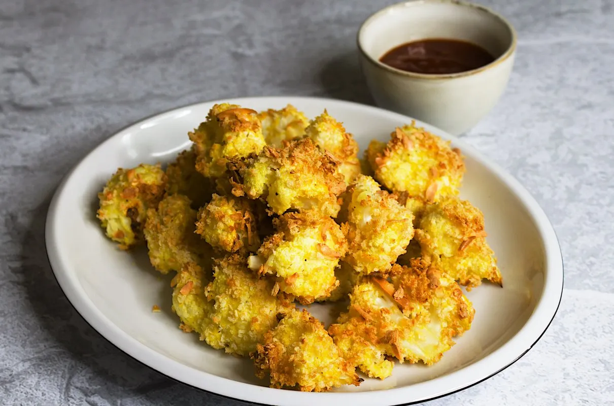 Chrupiące różyczki kalafiora w panko, złociste i apetyczne, podane na talerzu z sosem.