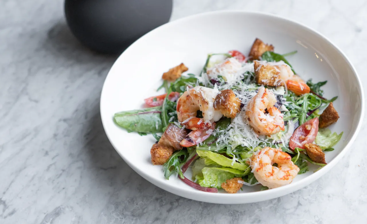 Pyszna sałatka cezar bez kurczaka z krewetkami, grzankami i parmezanem na białym talerzu.